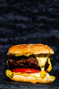 奶酪背景摄影照片_新鲜美味牛肉芝士汉堡的细节与黑色背景中突显的融化奶酪