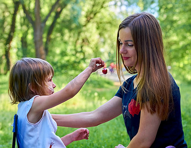 对待孩子摄影照片_一个可爱的孩子在大自然中用甜樱桃对待他心爱的母亲