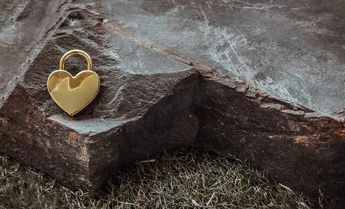 巨大心形背景摄影照片_在巨大的石头的金黄心形的爱挂锁在草背景。