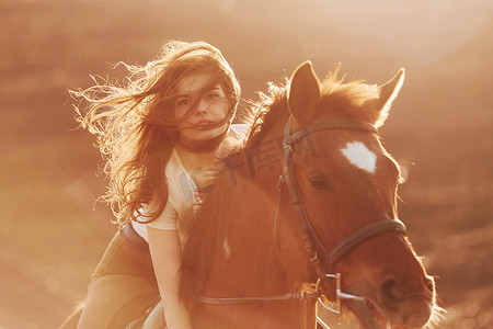 阳光明媚的白天，戴着防护帽的年轻女子和她的马在农田里