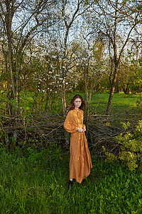 一位优雅、老练的女性身着橙色长裙，轻松地站在别墅的柳条栅栏旁，愉快地看着镜头