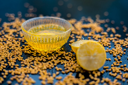 天然药摄影照片_著名的天然头皮屑在玻璃碗中的木制表面上的方法由胡芦巴种子粉与柠檬汁充分混合而成。表面上有生柠檬和胡芦巴种子。