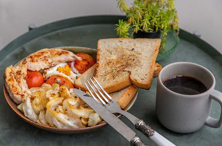 早餐包括烤鸡、煎蛋、西红柿、吐司面包和陶瓷盘上的炸卷心菜，搭配黑咖啡。