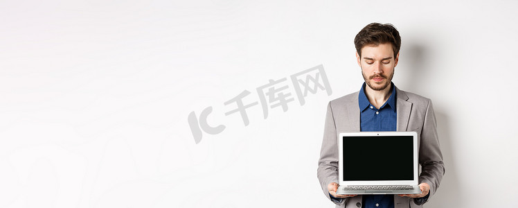 英俊的白人商人穿着西装，展示空的笔记本电脑屏幕，展示促销，站在白色背景上