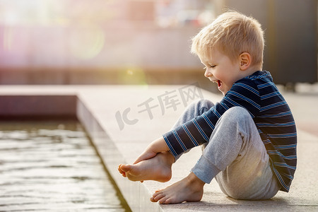 一个好奇的孩子，一个男孩，赤脚接触城市喷泉的水。