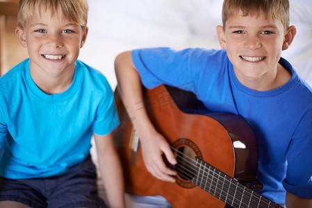 儿童歌摄影照片_教他弟弟唱几首歌……两个人坐在床上，一个人弹吉他。