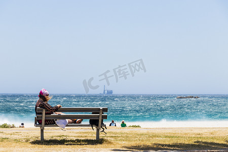 坎普斯湾 (Camps Bay) 风很大的海滩上坐在长椅上的女人。