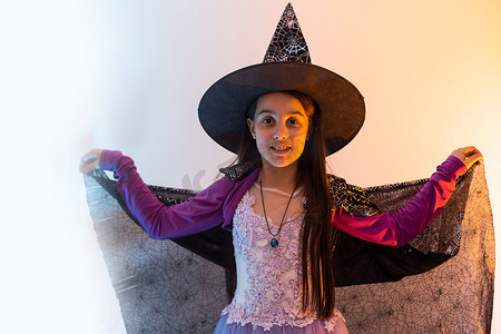 巫师摄影照片_戴着女巫帽的万圣节孩子看起来像巫师学校的学生，万圣节快乐。