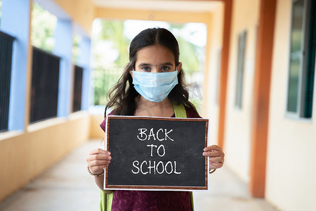 戴着医用面具的年轻女孩在走廊上背对着学校标牌 — 学校重新开放、生活方式和新常态的概念。