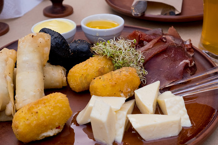 面糊摄影照片_粘土盘上的啤酒小吃：bastruma、feta 奶酪、面糊中的奶酪、蜂蜜和芥末。
