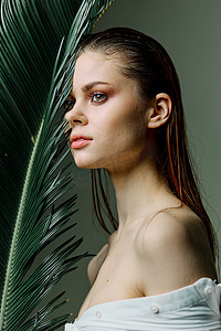 一位优雅女性的垂直照片肖像，她的头发向后梳，手拿棕榈叶靠近脸