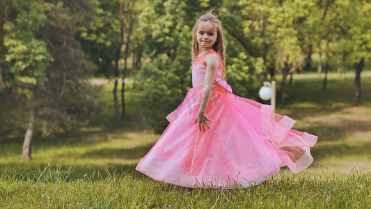 一个穿着粉红色公主裙的女孩正在公园里纺纱。