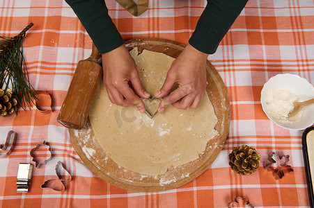 女厨师糖果手在姜饼面团上切心形模具，制作自制糕点的顶视图