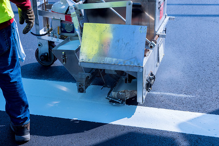 工人们用白色油漆在条纹上涂上道路标记，并在沥青上撒上反光粉