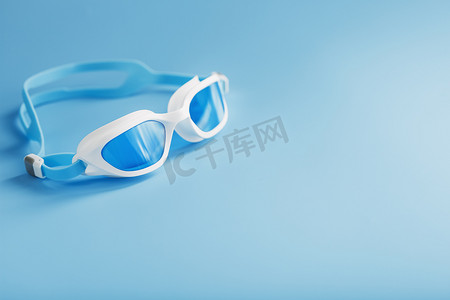 游泳泳镜摄影照片_蓝色背景中的白色泳镜