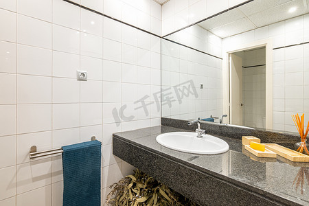 宽敞浴室的镜面景观配有大石台面镜子和墙上贴有反光白色瓷砖的水槽。