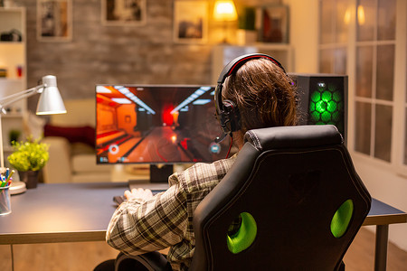 游戏玩家深夜在客厅里用他强大的 PC 电脑玩射击游戏的后视图