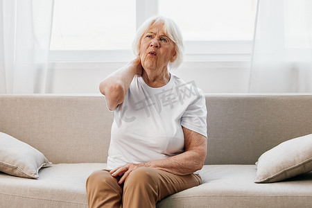 老年妇女坐在沙发上颈部严重疼痛，晚年健康问题，生活质量差。