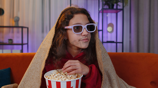 电影视频片摄影照片_Oreteen 女孩吃爆米花，在家里的沙发上看有趣的电视连续剧、体育游戏在线内容
