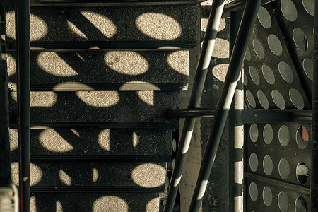 阳光的影子从建筑物金属板上的圆孔照到防火梯上。