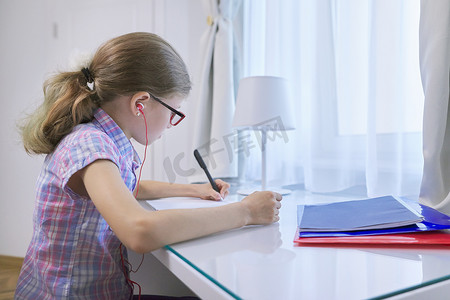 女童坐在家里靠近窗边的办公桌前，在笔记本上写字