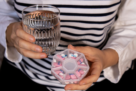 女手分拣药片组织者每周拍摄一杯水特写药盒，里面装有药片，每天服用白色粉红色药物和胶囊。