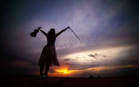 日落时分，头发松散的浪漫年轻女子在田野里拿着小提琴