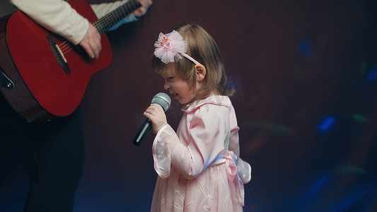 穿着复古裙子的小女孩在舞台上唱歌，她的父亲弹着原声吉他