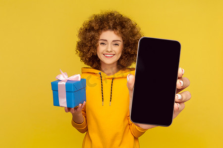 可爱高兴的女人拿着礼物盒，展示大空手机展示广告。