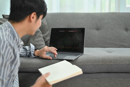 交易进行中摄影照片_男交易员投资者分析师看着笔记本电脑屏幕分析投资策略，在家进行交易