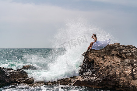 海中石头摄影照片_暴风雨中的女人坐在海中的一块石头上。