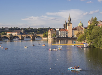 伏尔塔瓦河上的查理大桥全景和捷克共和国布拉格老城区的房屋，黄金时段的灯光，夏日阳光明媚的日子，游客在脚踏船上放松