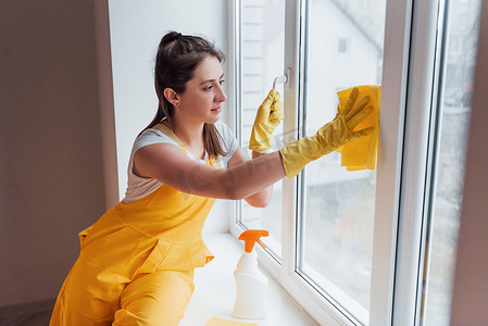 黄色制服清洁窗户的主妇。