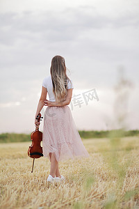 浪漫的年轻女人，头发飘逸，手里拿着小提琴，在田野里