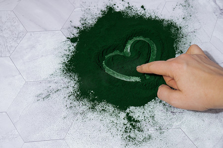 爱心手托卡通摄影照片_女手在蓝绿藻小球藻和螺旋藻粉上画心。