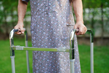 散步摄影照片_亚洲老年妇女残疾患者与助行器一起在公园散步，医学概念。