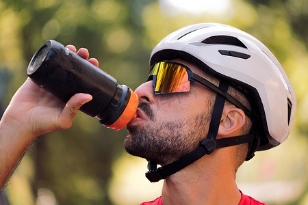 戴头盔和骑自行车护目镜喝水的人