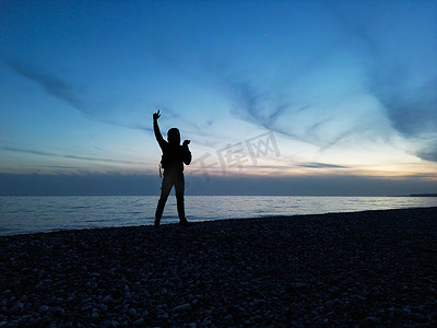 无人机剪影摄影照片_一个人在美丽的夕阳下以大海和云彩为背景的剪影在他手中是无人机的遥控器