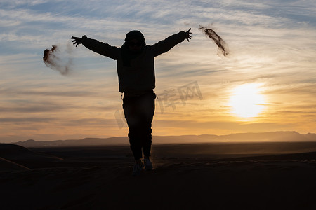 夕阳下在撒哈拉沙漠中跳跃和扔沙子的人的剪影