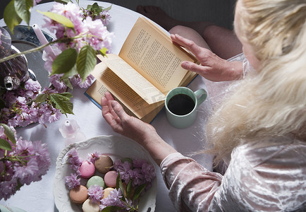 俯视角度的书摄影照片_身穿粉色裙子的金发女郎喝咖啡，为她的博客拍摄视频，从一个角度看，