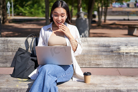 亚洲年轻女性与笔记本电脑进行视频聊天，坐在长椅上，远程进行在线会议