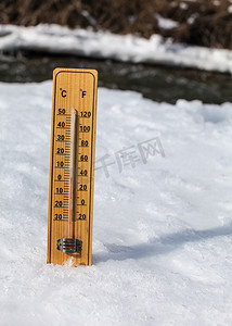 木制温度计站在部分结冰的河流的冰上，阳光明媚，显示 +3 度。
