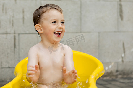 小男孩在洗澡摄影照片_可爱的小男孩在户外的黄色浴缸里洗澡。
