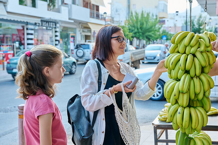母亲和女儿在街头零售市场购买农场香蕉。