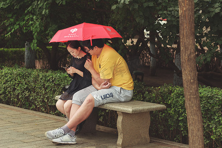 坐在长凳上的人摄影照片_伞下坐在长凳上的情侣