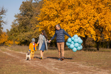 一个年轻的幸福家庭，带着小孩和狗一起在秋季公园散步