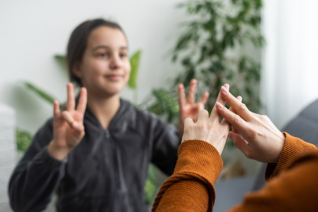 女儿用手语与中年母亲交谈，家人坐在扶手椅侧视，老师教青少年聋哑女孩视觉手手势符号概念形象