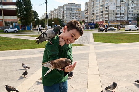 微笑可爱的白人少年，在城市广场喂岩鸽时表达积极情绪