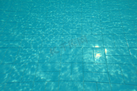 游泳池底部，阳光照在蓝色瓷砖上，水折射扭曲的线条。