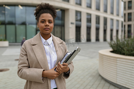一名非裔美国人长相的女性，一名官员站在行政大楼的背景下，手里拿着笔记本电脑和文件